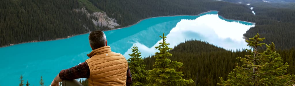 man sitting on cliff looking can the icy blue water below.
