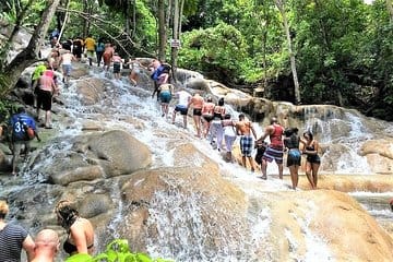 waterfall with people climbing up it holding onto a rope.