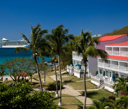 caribbean red roofed and white building resort with palm trees and the sea in the background
