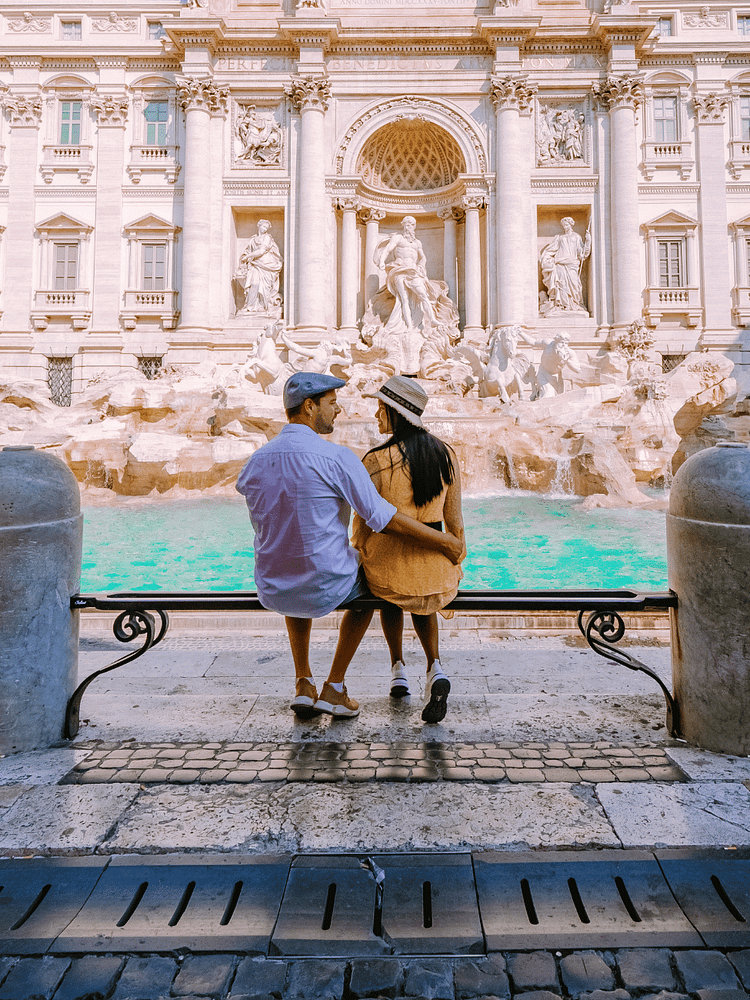 couple sitting on bench in front of the Trevi fountain in Rome