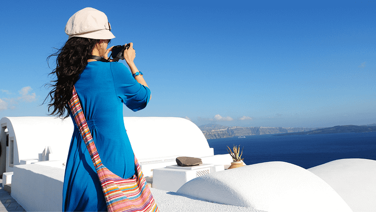 Woman in blue looking out on the blue horizon while standing on the roof of a white building