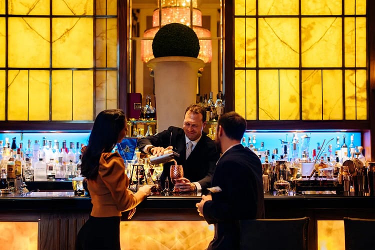 Rome Luxury bar with yellow goldish decor bartender is serving couple mixed drinks.  